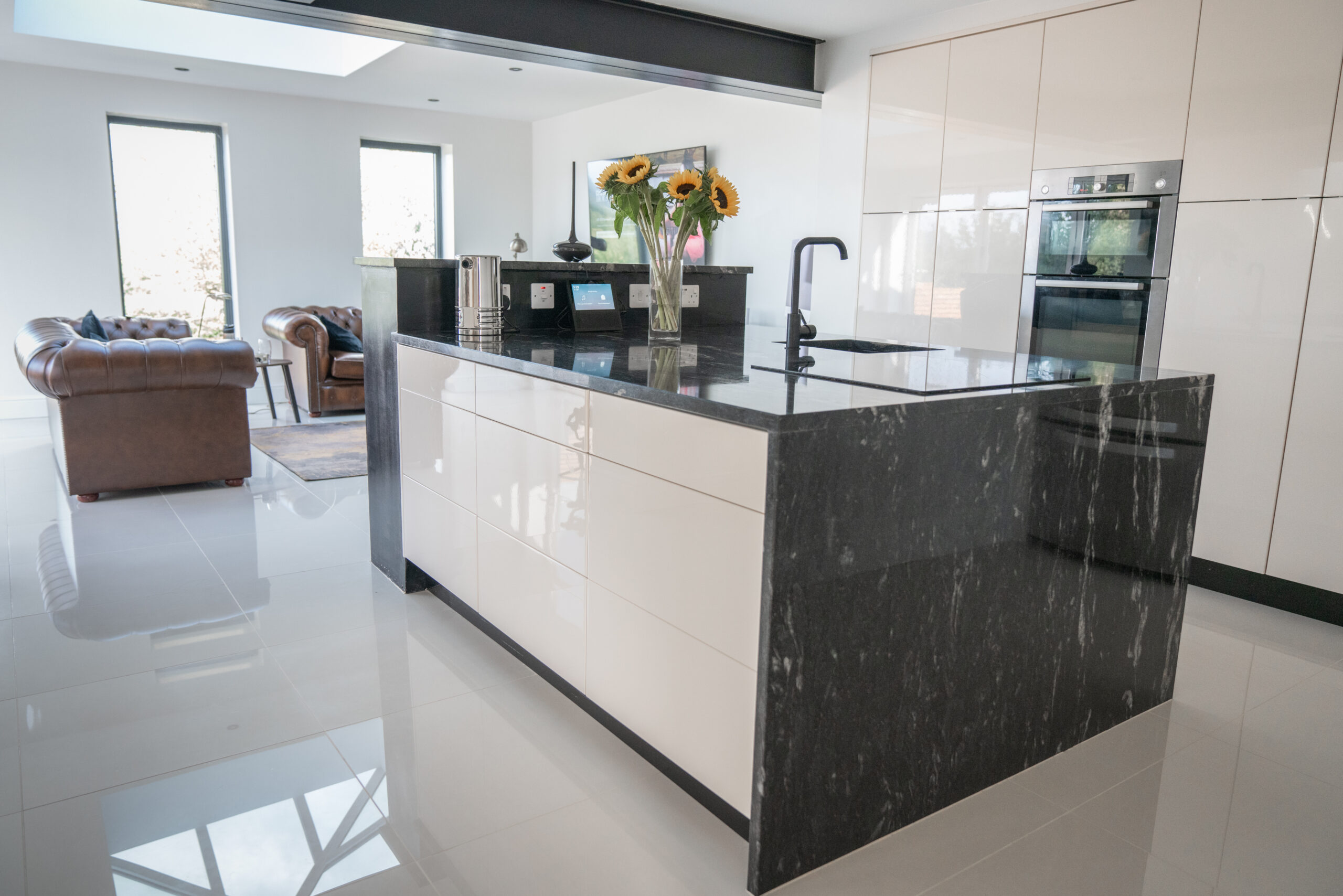 Side view of a modern kitchen with Cosmic Black Granite worktops on the island and perimeter run, showing waterfall ends and a polished surface finish.