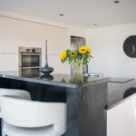 Wide view of a modern kitchen island in Cosmic Black Granite with a polished finish, showing an overhang with seating and sunflowers on the worktop.