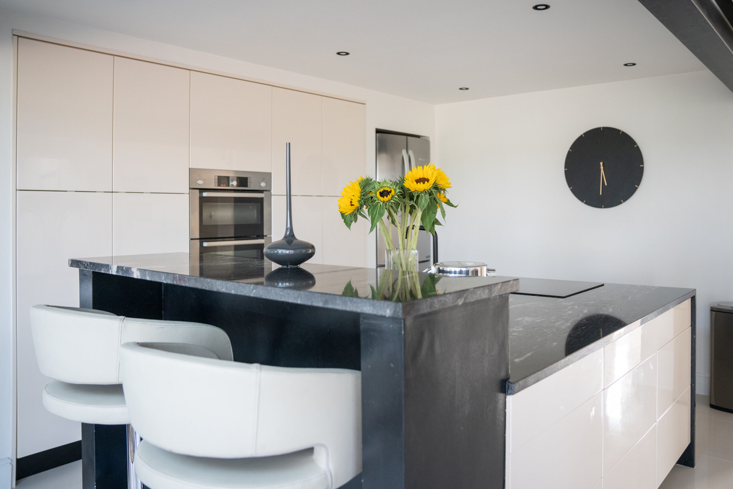 Wide view of a modern kitchen island in Cosmic Black Granite with a polished finish, showing an overhang with seating and sunflowers on the worktop.