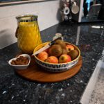 Styled close up of Blue Pearl Granite worktop with a breakfast tray, fruit bowl and orange juice, showing the dark speckled Granite pattern.