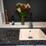 Sink area in Blue Pearl Granite with a white inset sink and black tap, showing the speckled Granite surface and a vase of flowers by the splashback.