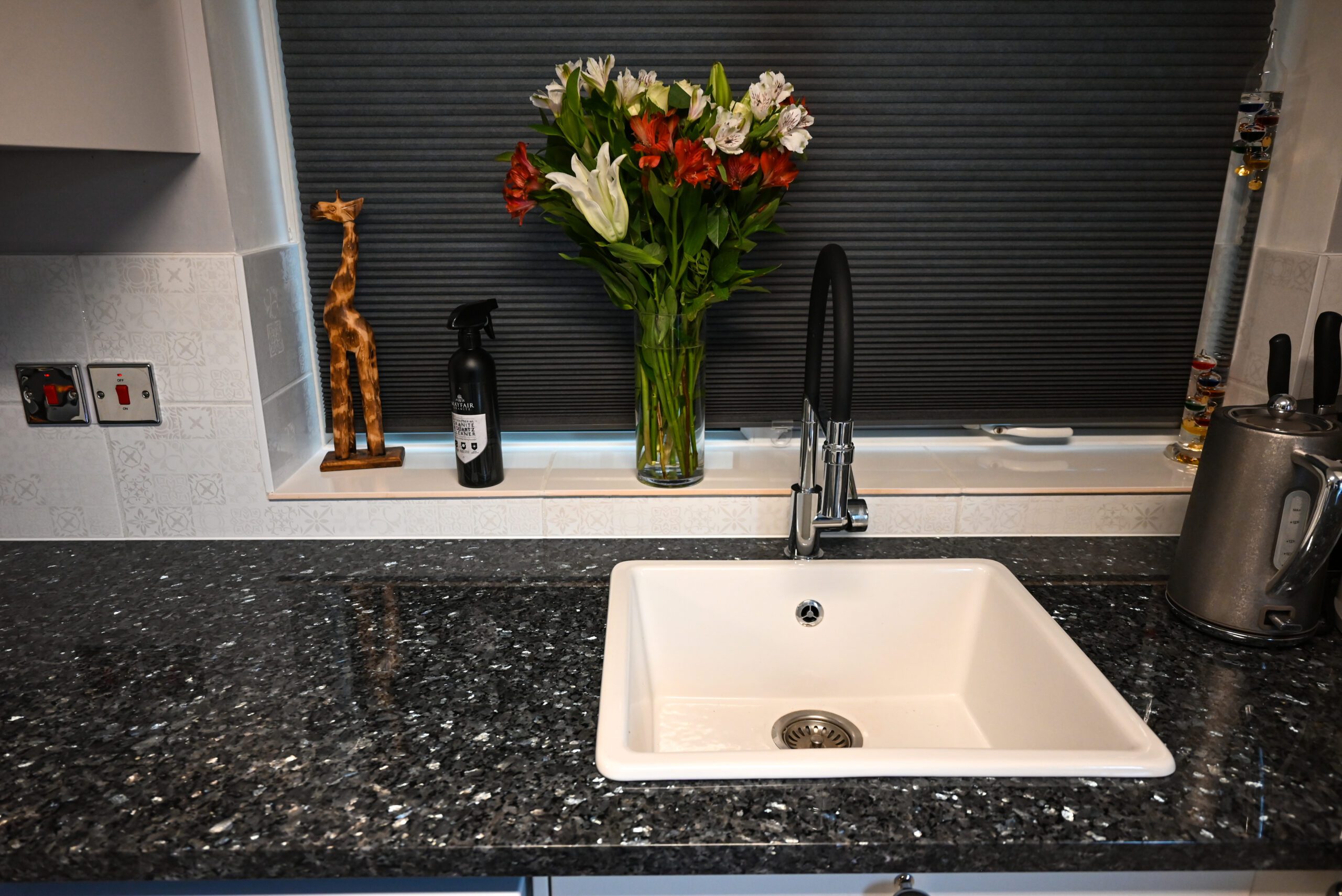 Sink area in Blue Pearl Granite with a white inset sink and black tap, showing the speckled Granite surface and a vase of flowers by the splashback.