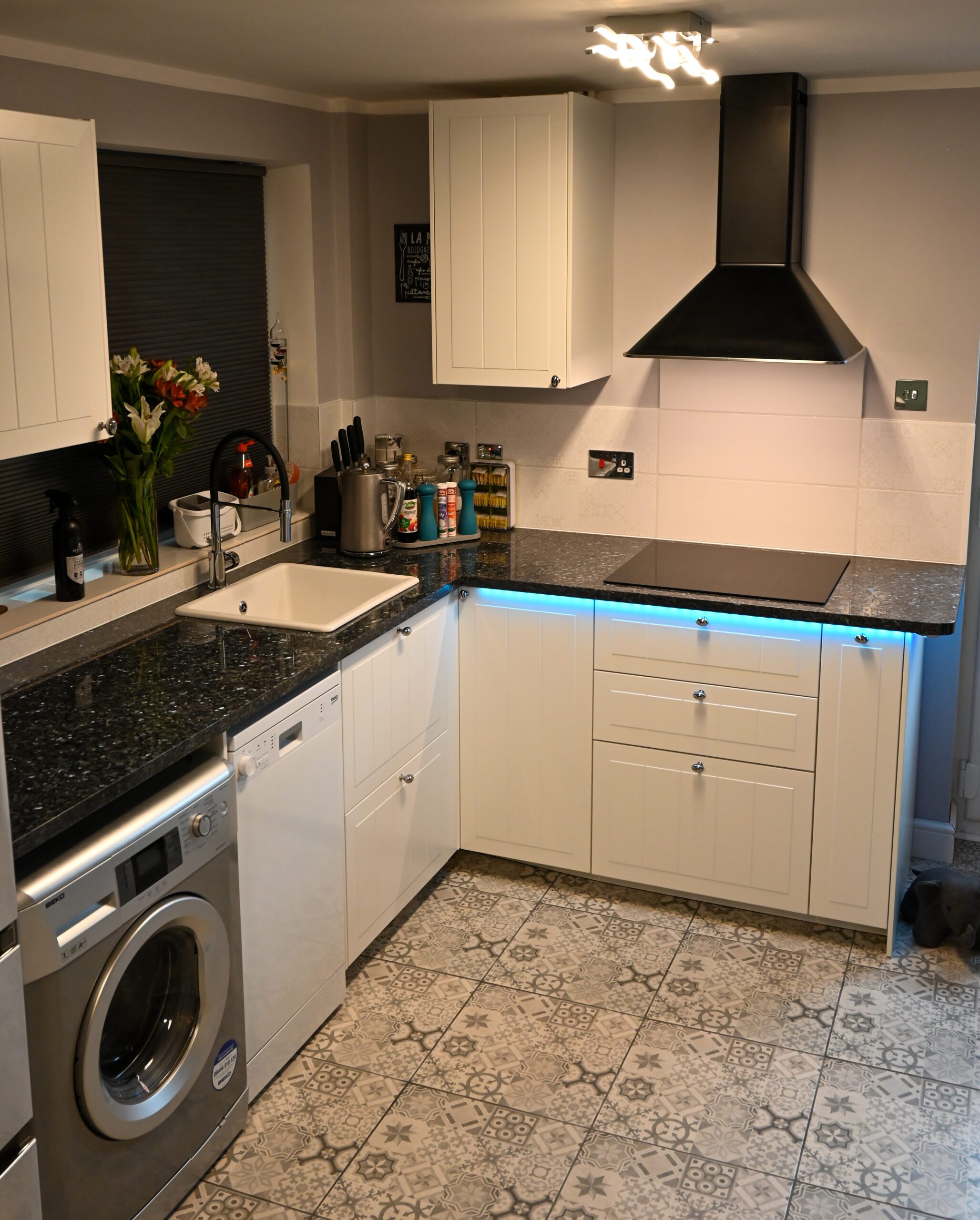 Open plan kitchen angle showing Blue Pearl Granite worktops on white cabinetry, with under cabinet lighting and the speckled Granite surface along the run.