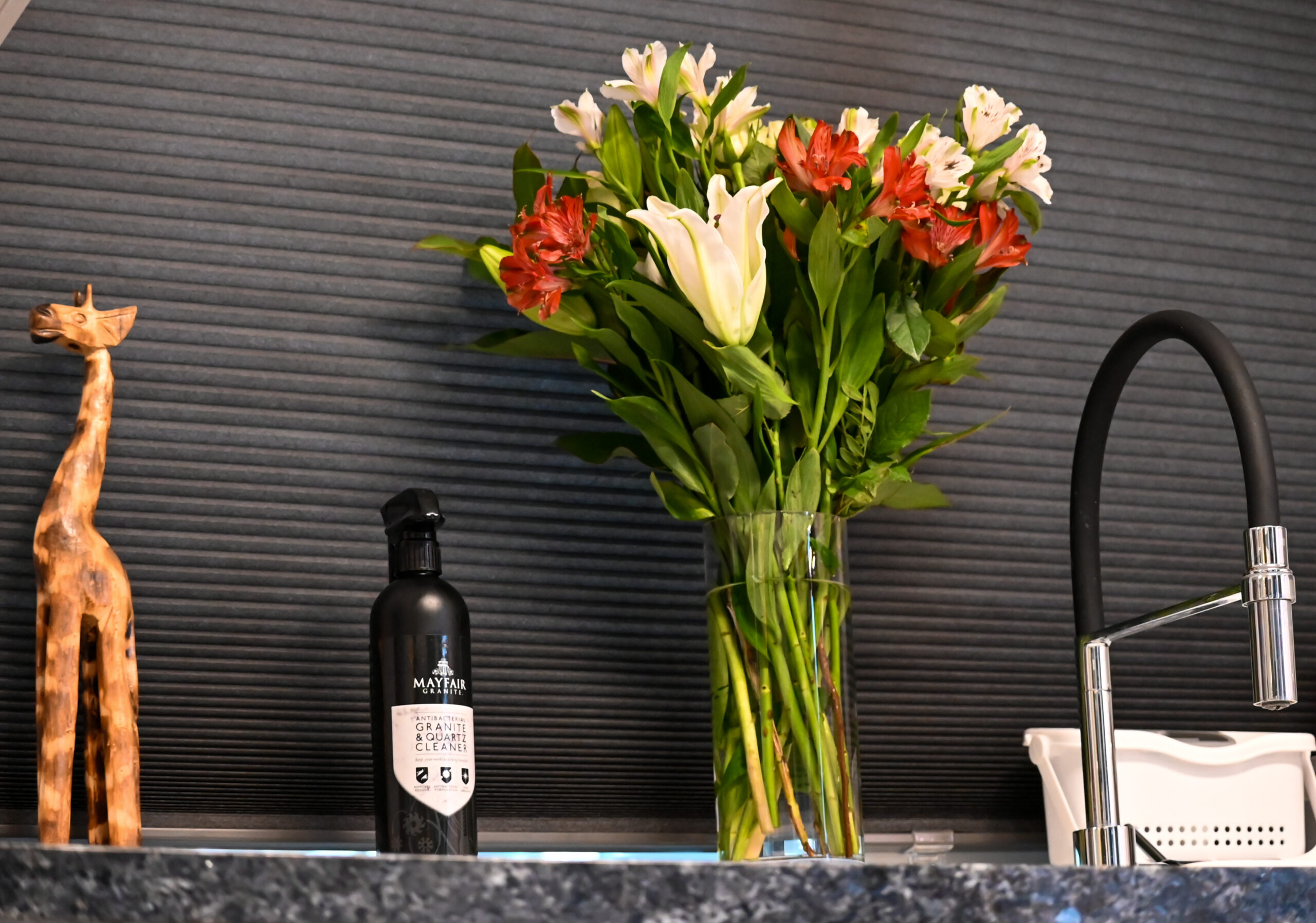 Blue Pearl Granite worktop detail with a vase of flowers and a wine bottle, showing the speckled Granite surface against a dark splashback.