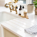 Ice White Quartz drainer grooves beside a white sink with brass taps and a drying rack on the surface