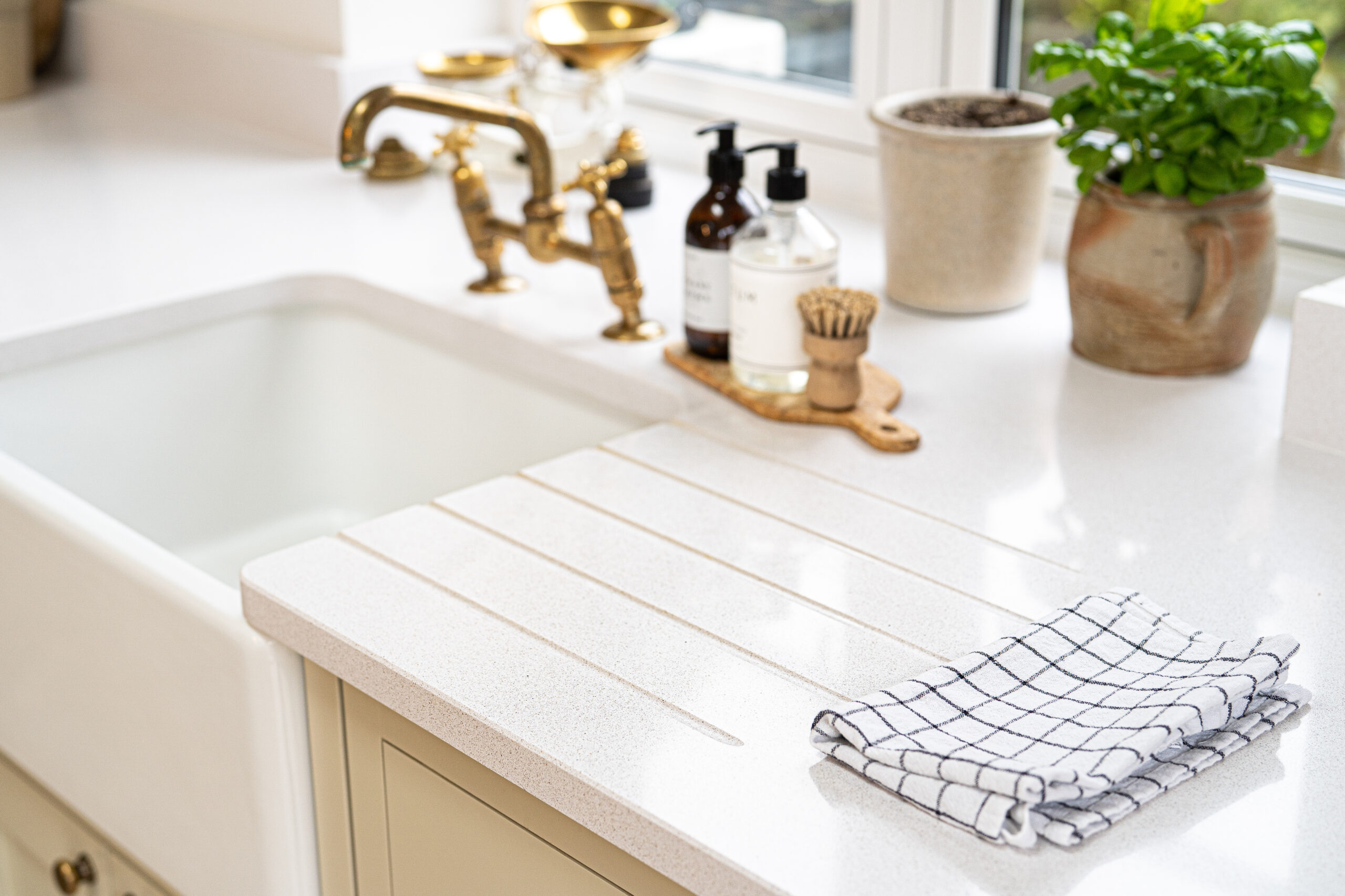 Ice White Quartz drainer grooves beside a white sink with brass taps and a drying rack on the surface