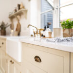 Ice White Quartz worktop on a sink run with a farmhouse sink and brass tap in a bright kitchen