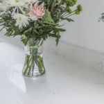 Close-up of Bluetta Carrara Quartz worktop surface with flowers in a vase, showing subtle grey veining