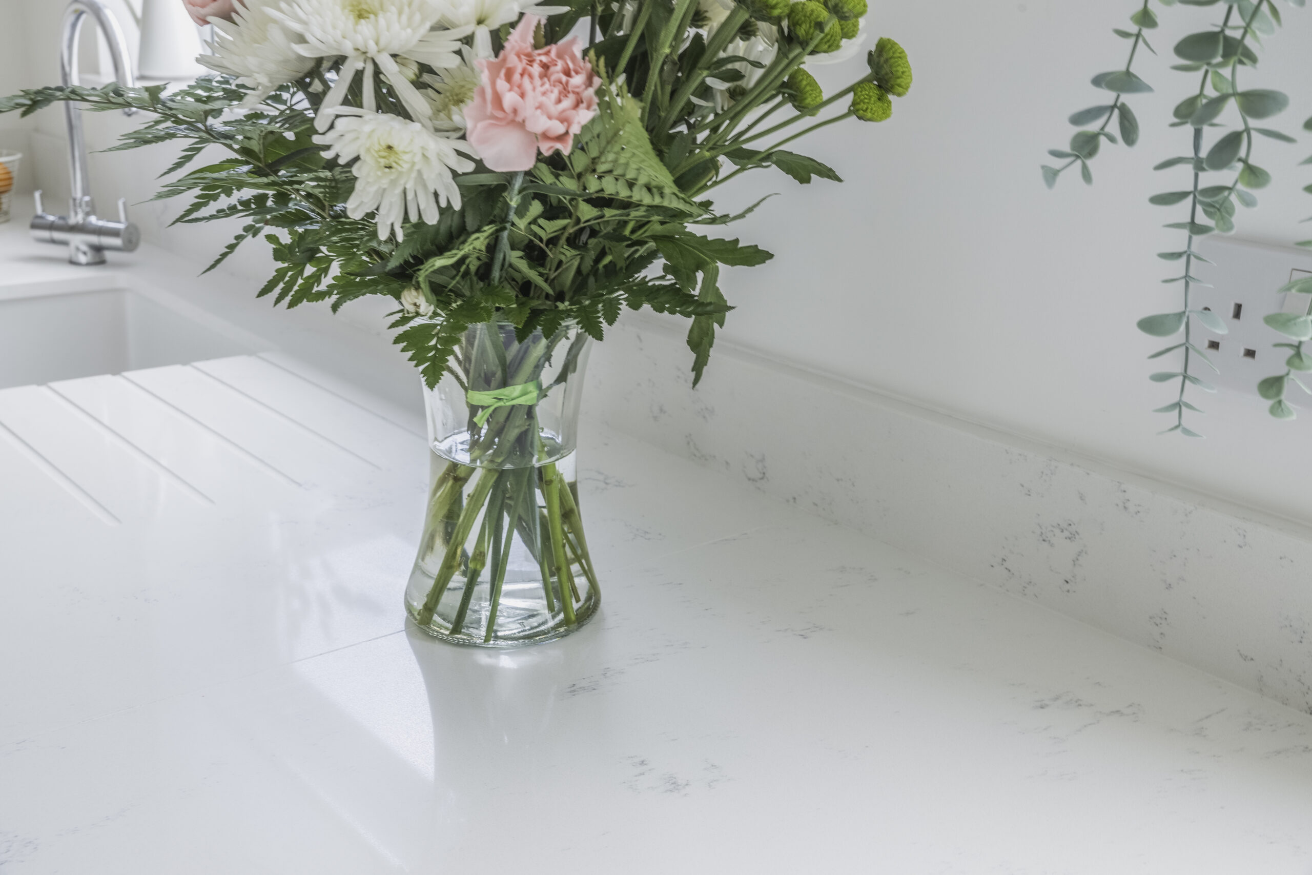 Close-up of Bluetta Carrara Quartz worktop surface with flowers in a vase, showing subtle grey veining