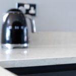 Grey Drift Quartz worktop close-up with kettle in the background showing a light grey stone-effect finish