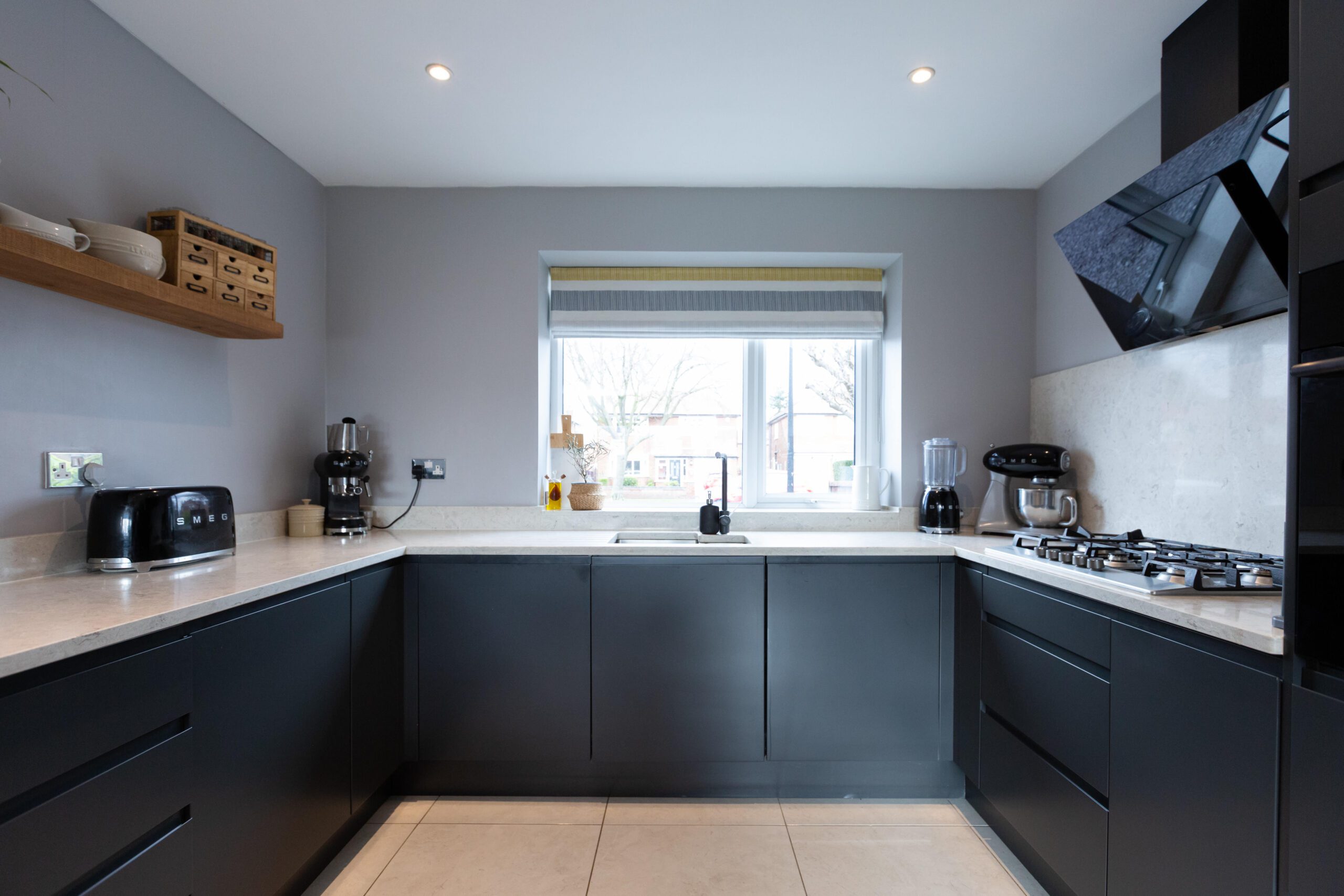 Grey Drift Quartz worktops fitted to a U-shaped kitchen with a window sink area and dark cabinetry