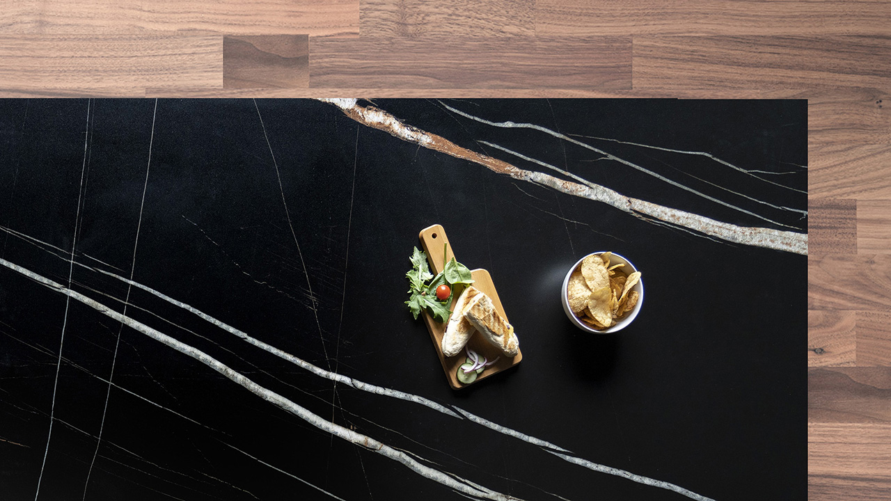 Noir St Laurent Porcelain worktop slab close up showing deep black surface with bold gold veining, styled with food and accessories