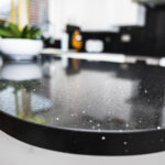 Black Starlight Quartz island edge close-up showing a curved front profile and sparkle flecks in the polished black surface