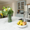 Arabescato Quartz island worktop with flowers and fruit bowl beside a sink, showing grey veining