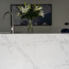 White Calacatta Quartz waterfall island showing grey veining with chrome tap and flowers in the background