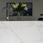 White Calacatta Quartz waterfall island showing grey veining with chrome tap and flowers in the background