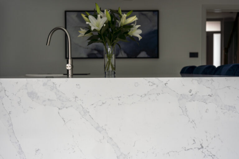 White Calacatta Quartz waterfall island showing grey veining with chrome tap and flowers in the background