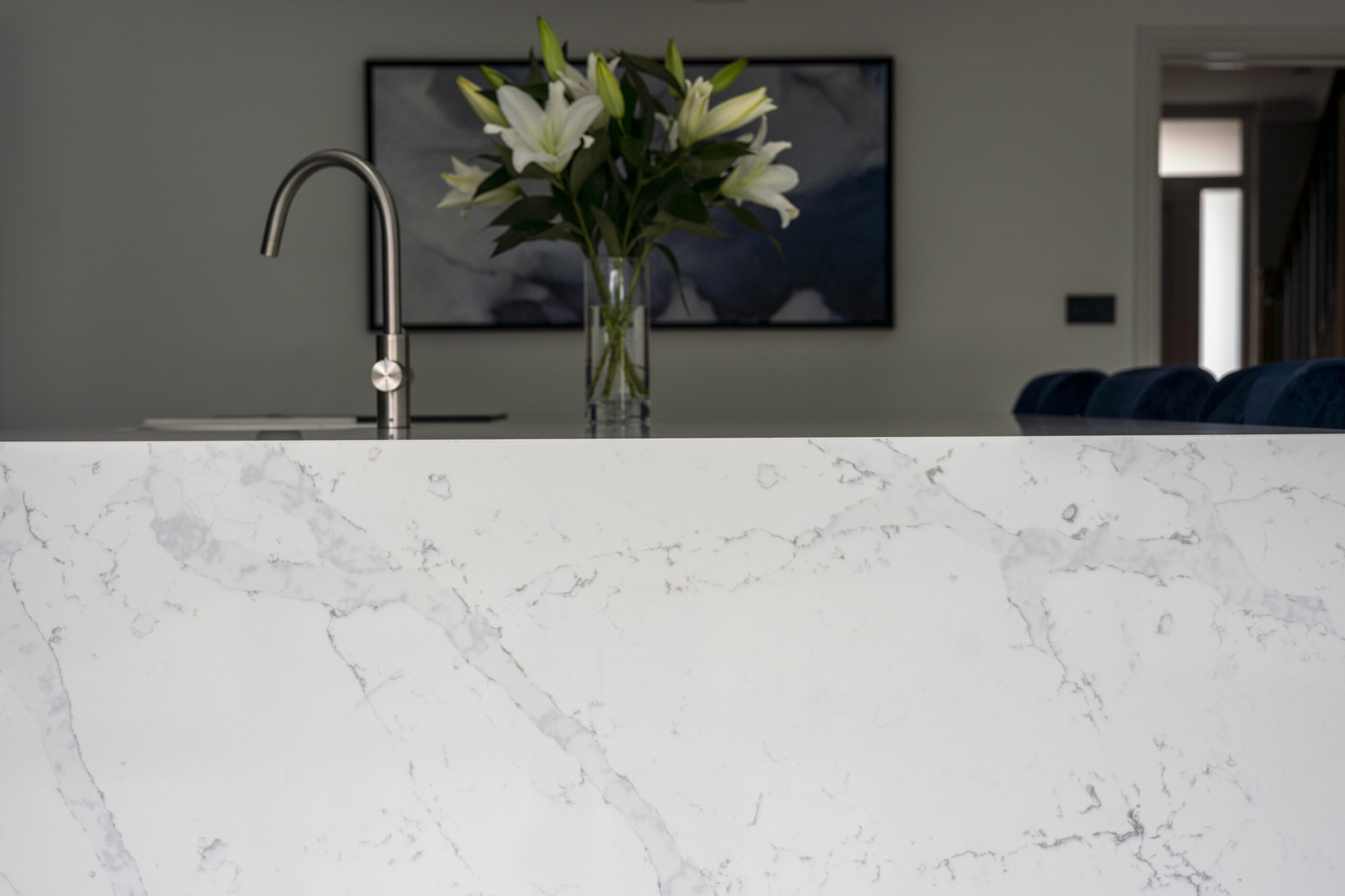 White Calacatta Quartz waterfall island showing grey veining with chrome tap and flowers in the background