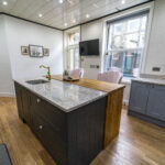 Angled island shot of Ivory Fantasy Granite worktops with dark base units and timber flooring, showing the full run and edge detail.