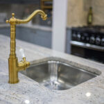 Kitchen sink detail with brass tap set into an Ivory Fantasy Granite worktop, highlighting the Granite pattern and smooth polished finish.