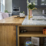 Island end view showing an Ivory Fantasy Granite worktop with inset sink, styled with flowers and accessories above open shelving.