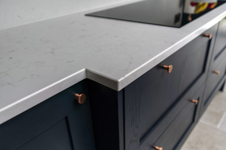 Carrara Quartz worktop on navy kitchen cabinets with copper handles