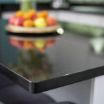 Close up of the polished edge of an Absolute Black Granite island worktop with a fruit bowl in the background, showing the deep black tone and glossy finish.