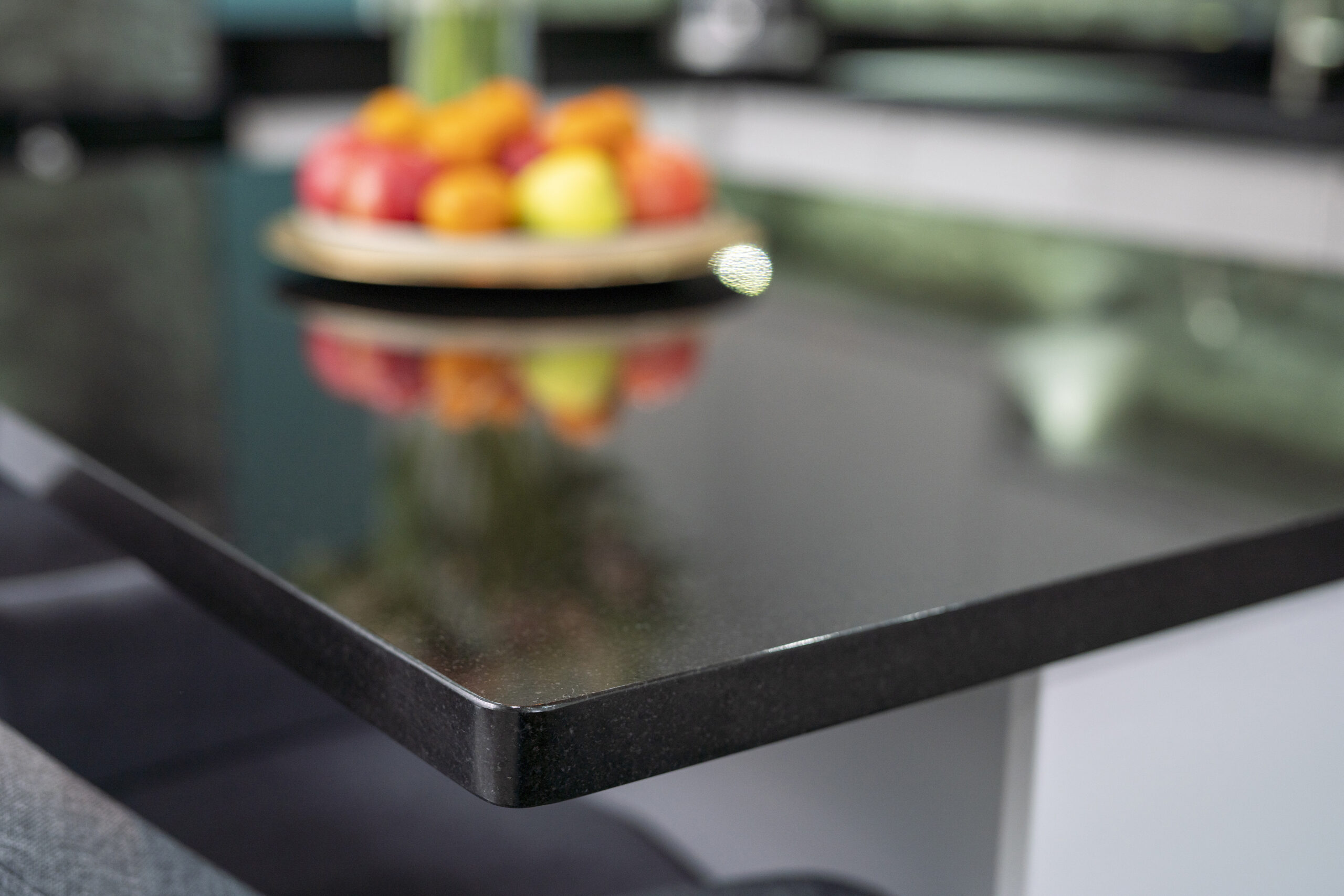 Close up of the polished edge of an Absolute Black Granite island worktop with a fruit bowl in the background, showing the deep black tone and glossy finish.