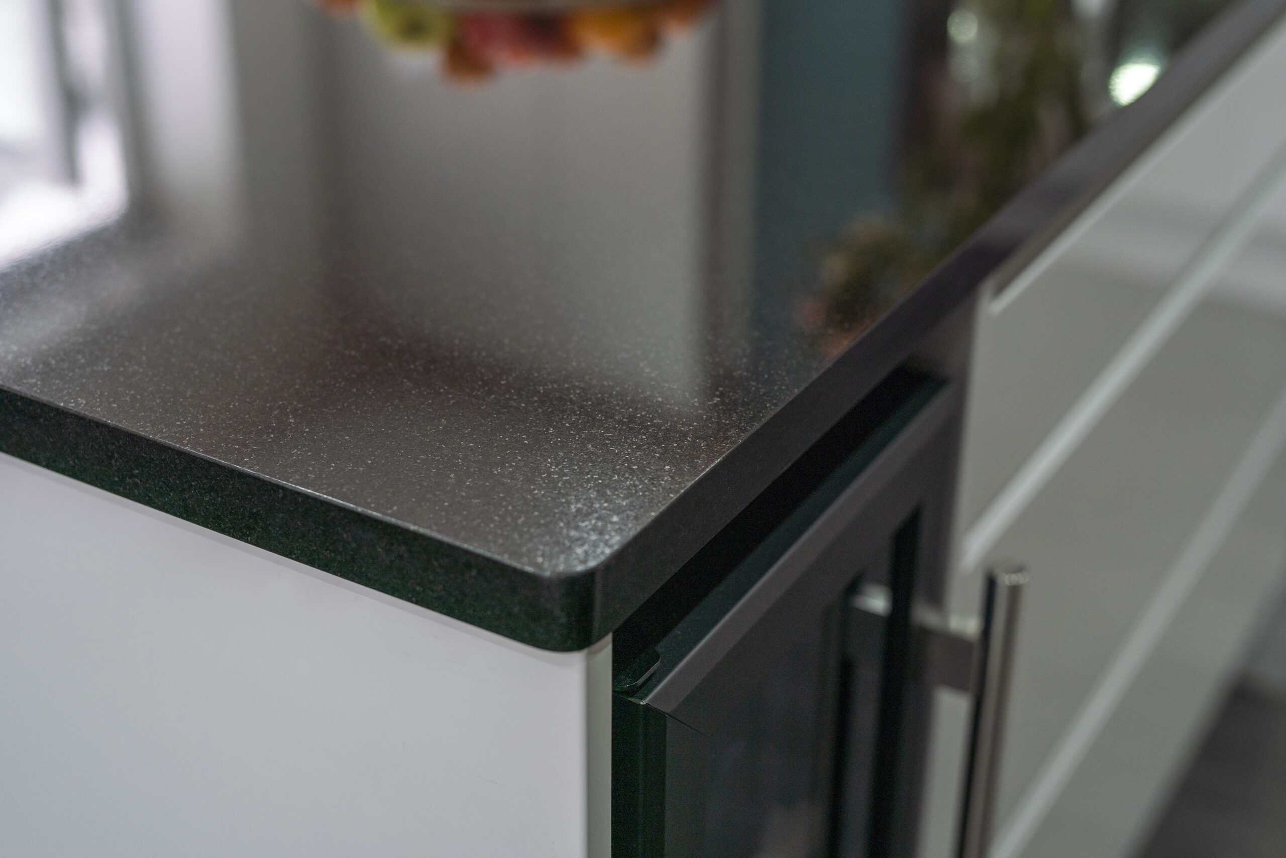 Close up of an Absolute Black Granite worktop corner with a polished edge, showing the end profile above a kitchen cupboard handle.