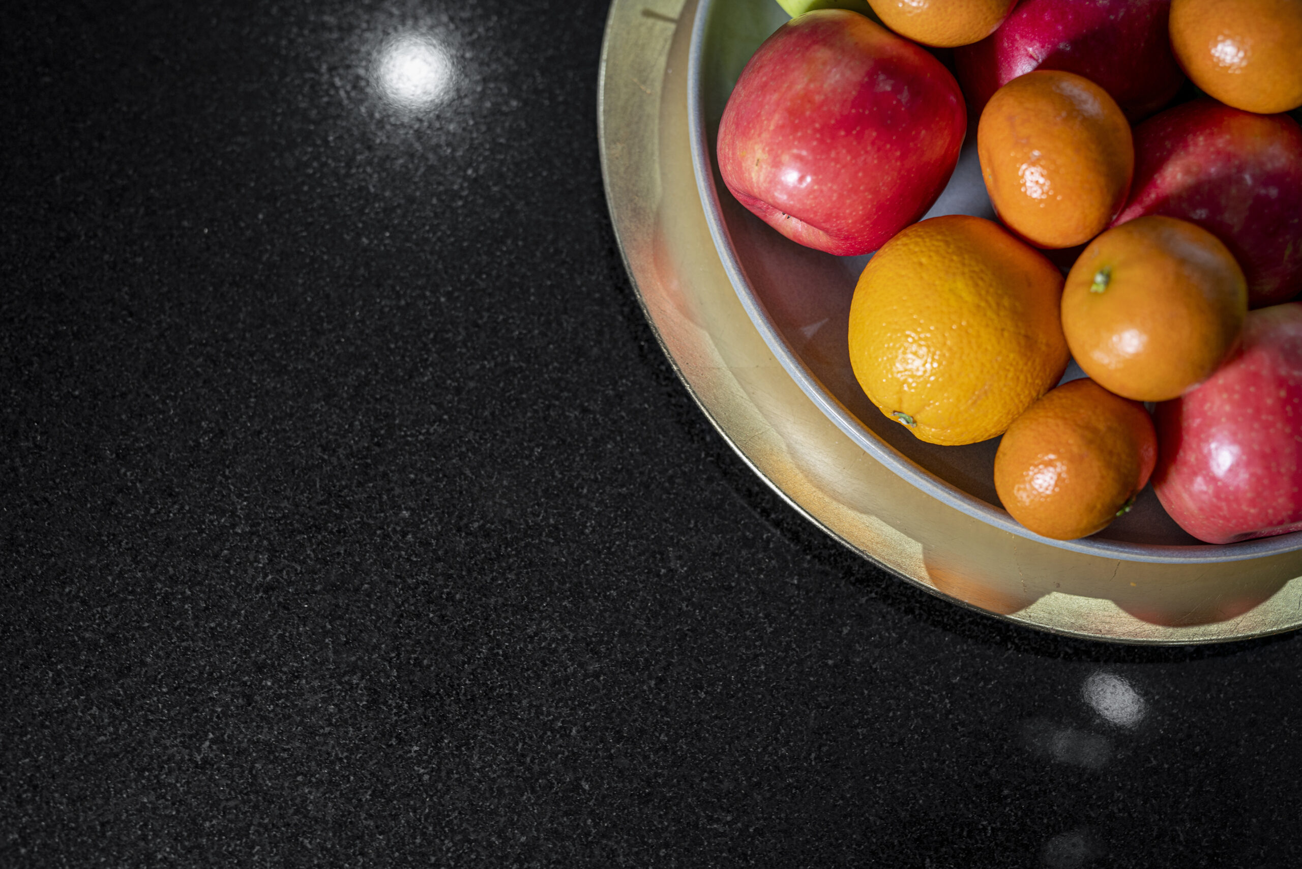Close up of Absolute Black Granite worktop surface with a bowl of fruit, showing the consistent black tone and light reflection on the polished finish.
