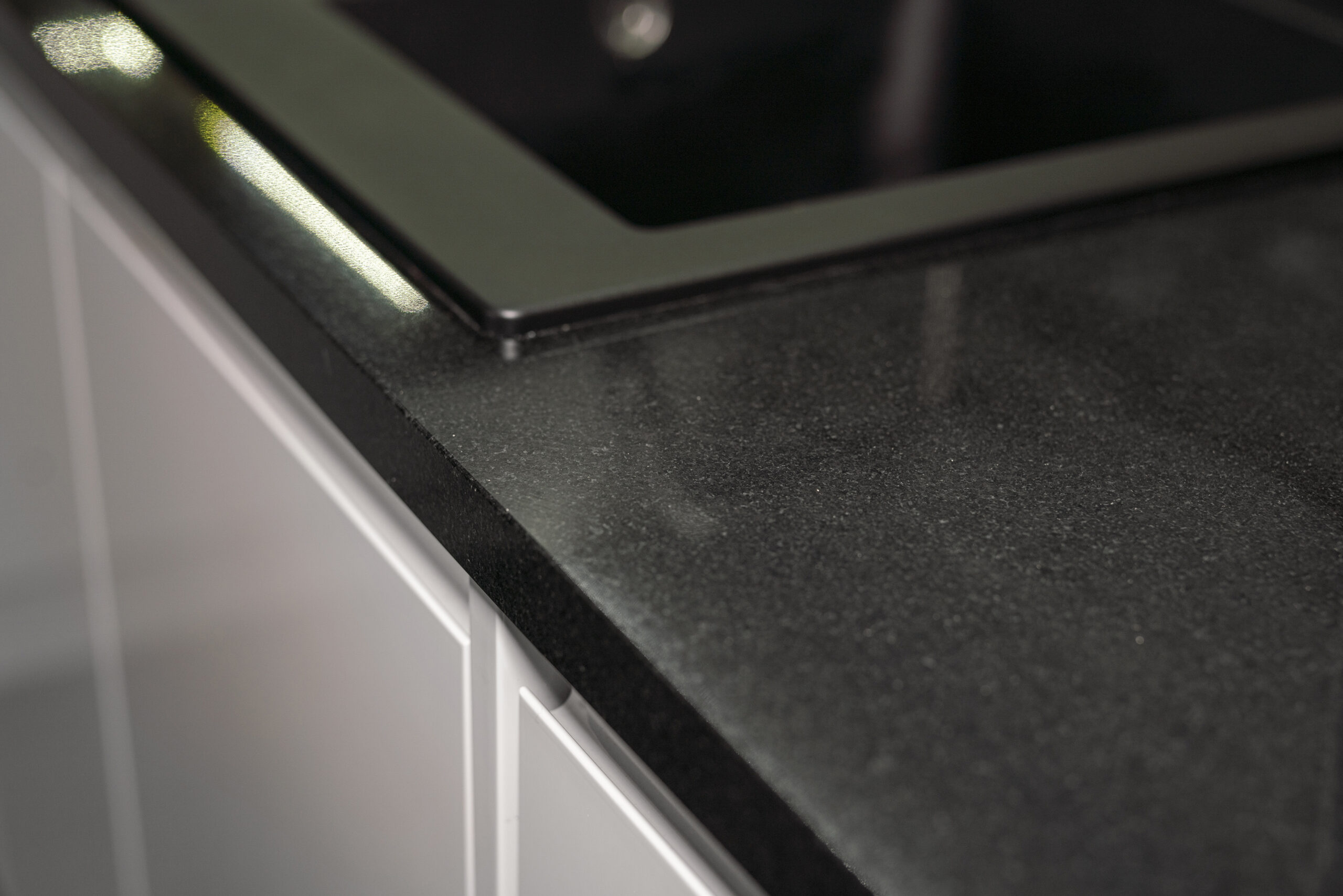 Close up of an Absolute Black Granite worktop corner with a polished finish, showing the edge detail beside an inset hob in a modern kitchen.