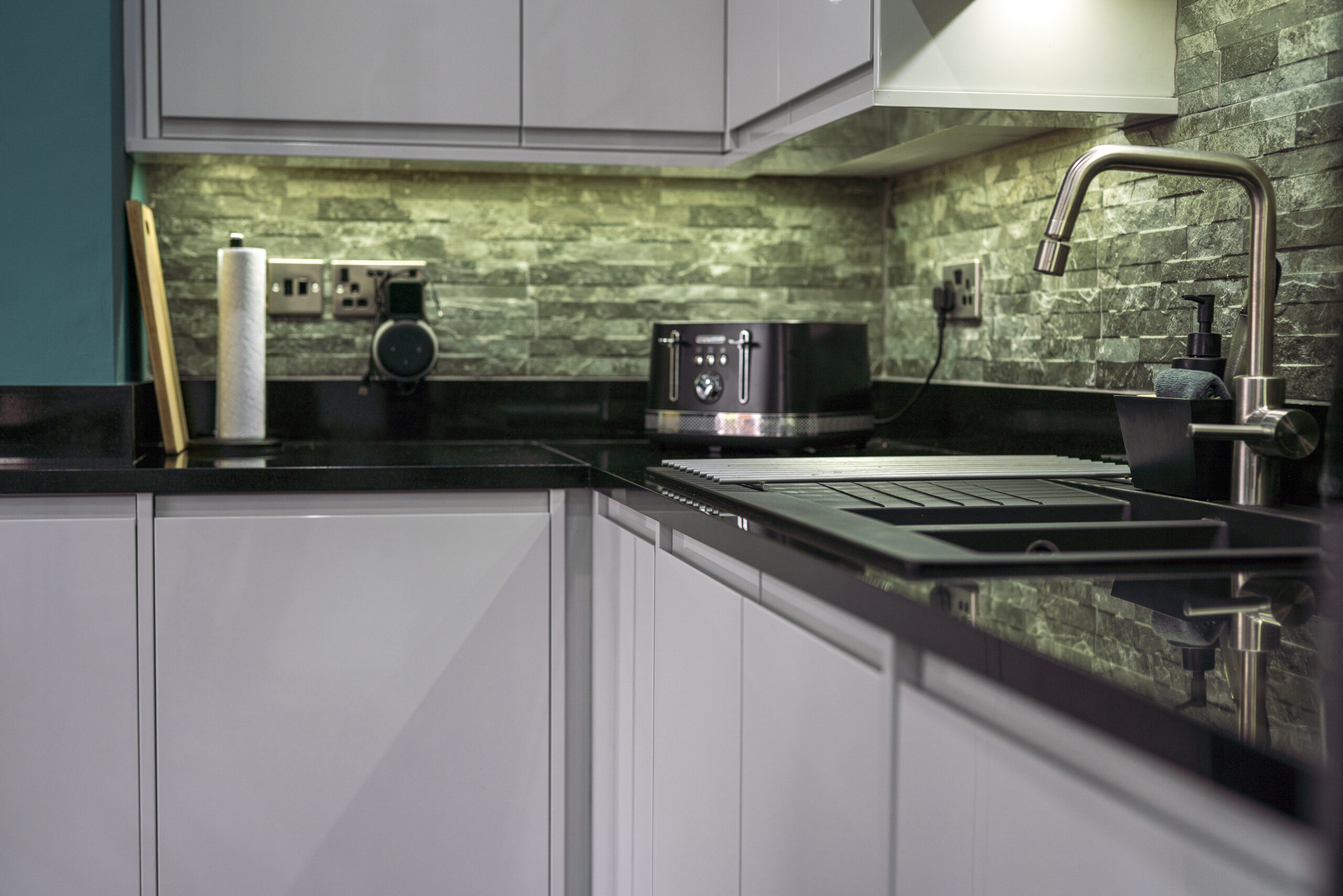Angled view of an L shaped kitchen with Absolute Black Granite worktops and matching upstand, showing the sink area and polished Granite surface.