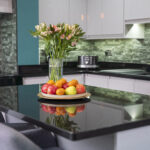 Modern kitchen scene with an Absolute Black Granite island worktop and curved corner, styled with fruit and flowers to show the polished surface.