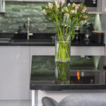 Close up of an Absolute Black Granite island worktop with a polished reflective finish, styled with a vase of flowers in a modern kitchen.