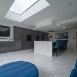 Modern open plan kitchen with White Calacatta Quartz island and blue bar stools under a large skylight