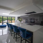 Modern open plan kitchen with White Calacatta Quartz island and blue bar stools under skylights