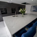 White Calacatta Quartz kitchen island with blue bar stools and floral arrangement on the worktop