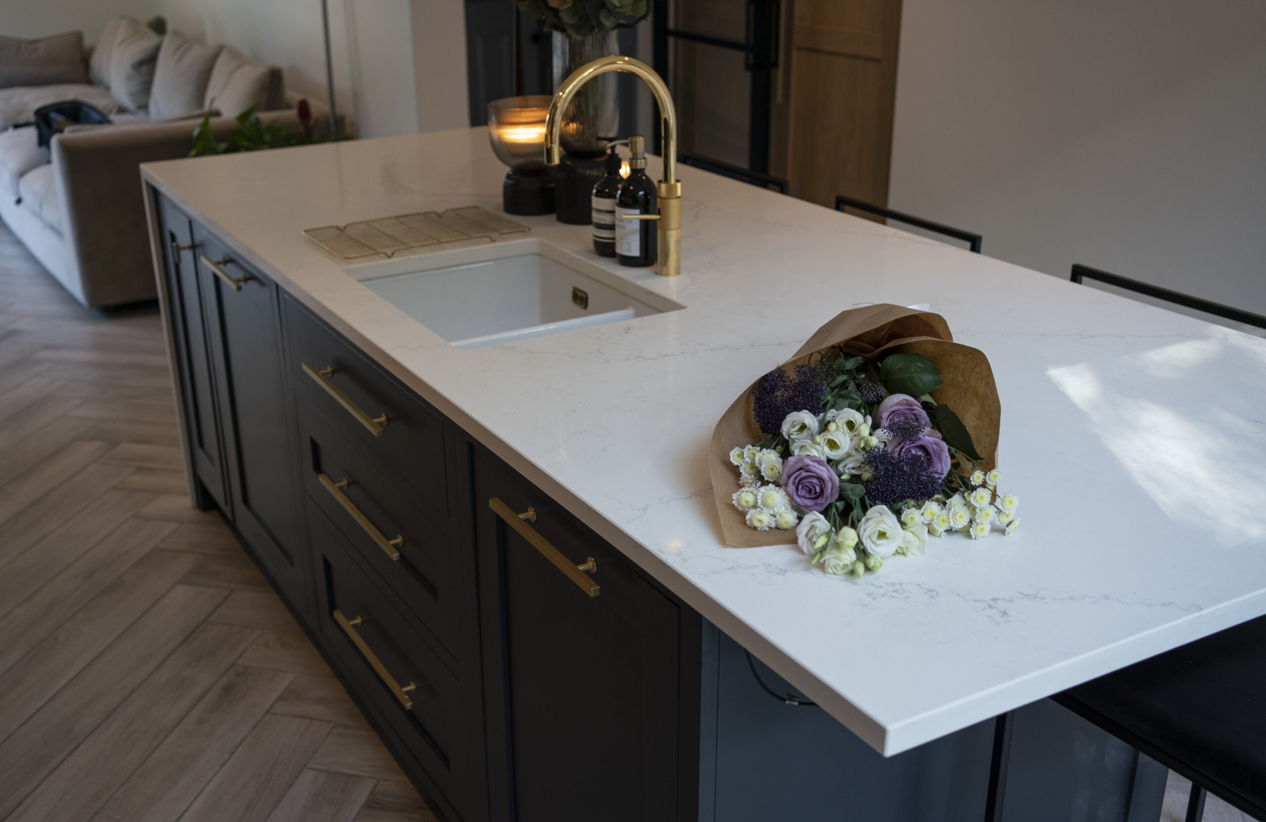 Olympus White Quartz island worktop shown with a brass tap and floral arrangement on the surface