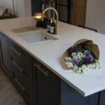 Olympus White Quartz island worktop shown with a brass tap and floral arrangement on the surface