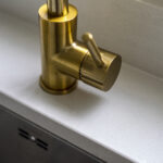 Brass tap detail set into an Imperial White Quartz worktop with a smooth white finish