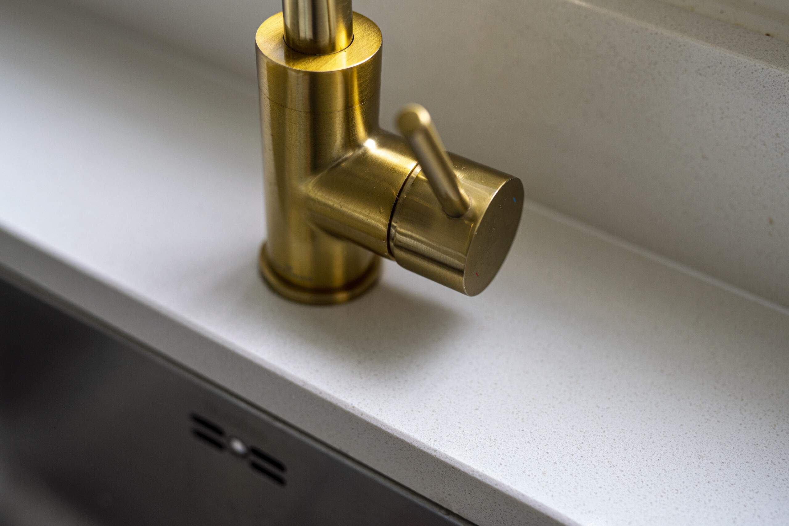 Brass tap detail set into an Imperial White Quartz worktop with a smooth white finish