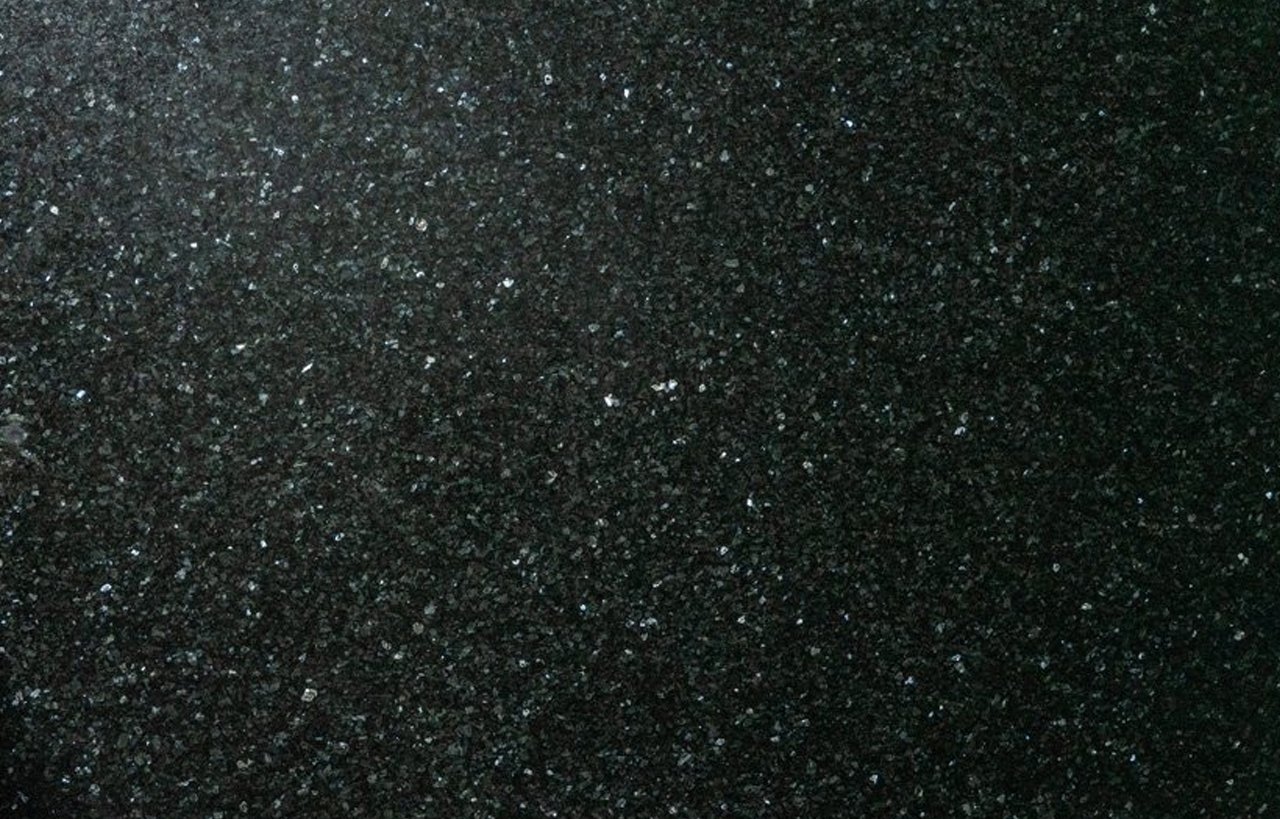 Close up slab photo of Emerald Pearl Granite showing a dark base with shimmering green and silver crystal flecks across the surface.