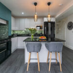 Front view of an Absolute Black Granite island worktop with breakfast bar seating, showing two grey stools, pendant lights and the polished Granite surface.