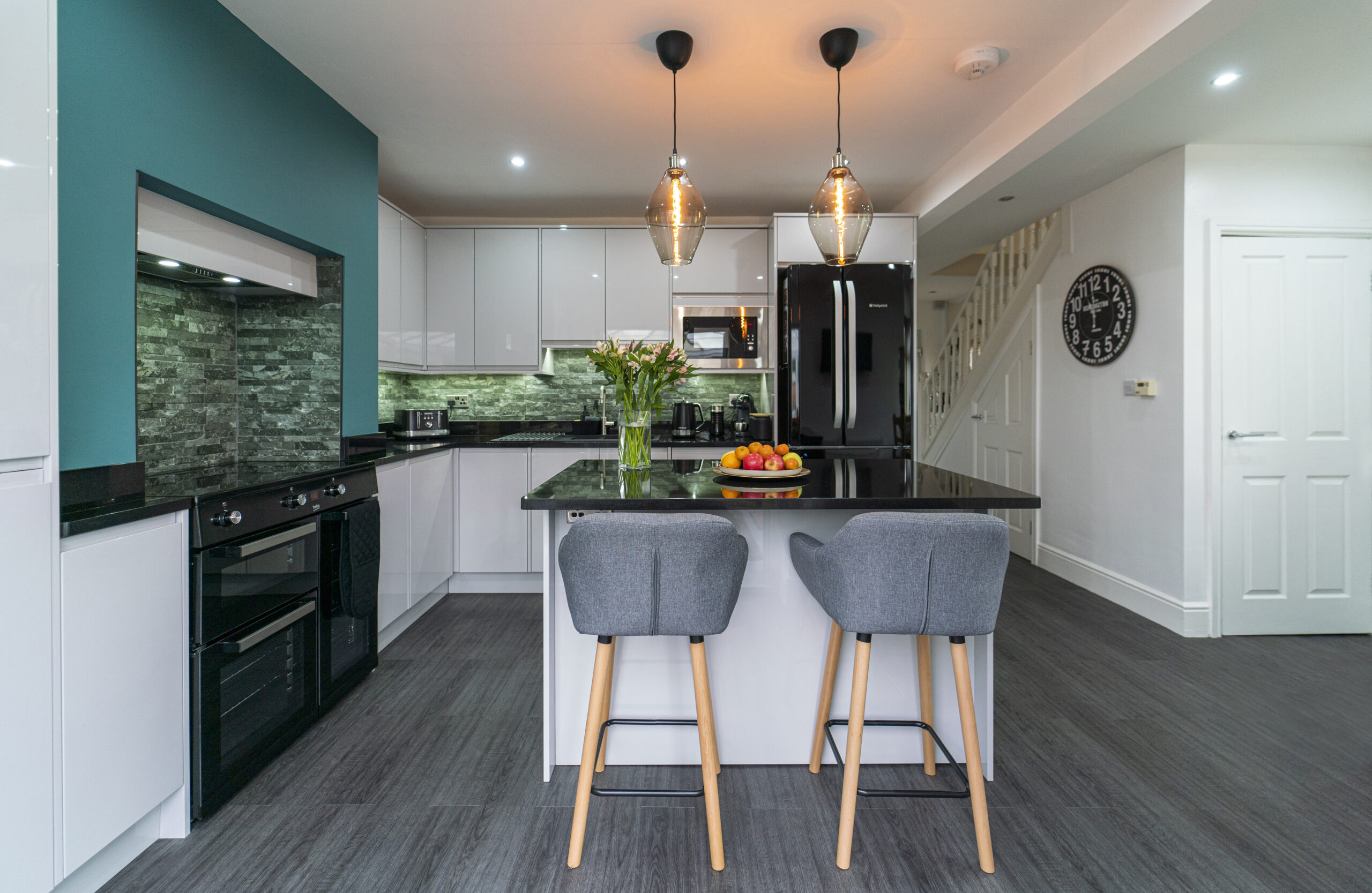 Front view of an Absolute Black Granite island worktop with breakfast bar seating, showing two grey stools, pendant lights and the polished Granite surface.