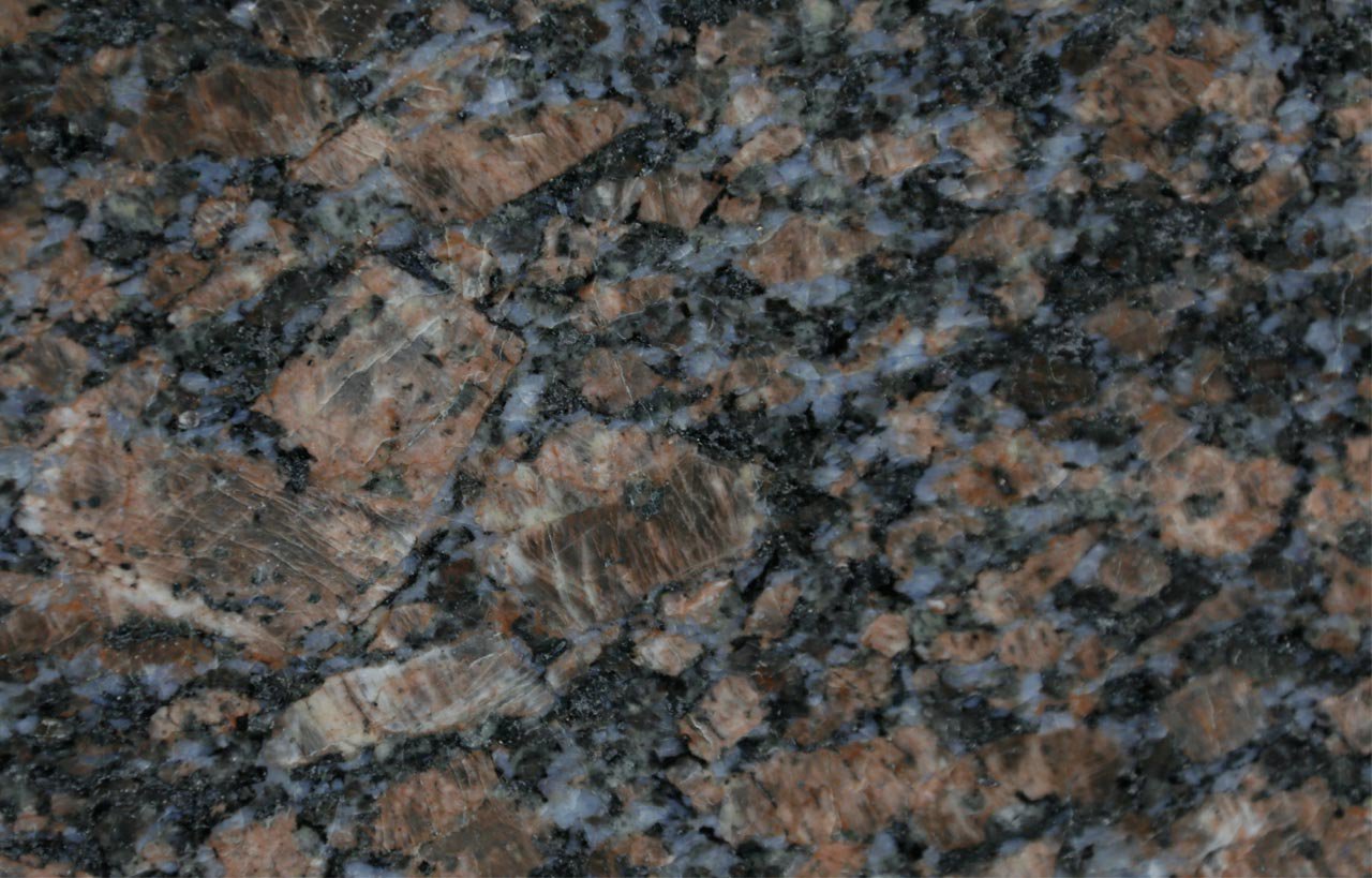 Close up slab photo of Sapphire Brown Granite showing a dense mix of brown, black and blue grey crystals with natural fleck patterning.