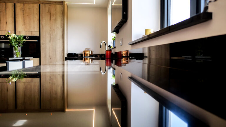 Side view along an Absolute Black Granite island worktop showing the polished edge detail with kitchen accessories on the surface and light reflecting off the Granite.