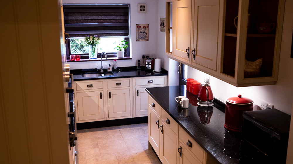 Wide view of a traditional kitchen with Star Galaxy Granite worktops on the perimeter run, showing the glossy black surface, sink area and light cabinetry.