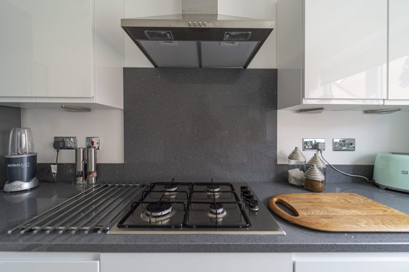 Grey speckled Quartz worktop with matching splashback behind a gas hob and cooker hood