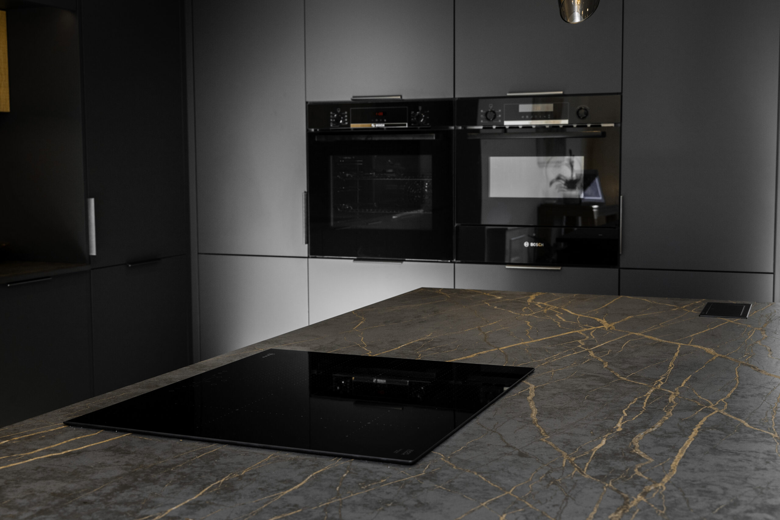 Laurent Porcelain island worktop with an inset induction hob, shown in a modern kitchen with tall units and built-in ovens.