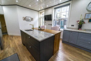 Wide angle view of an Ivory Fantasy Granite island worktop in a bright kitchen, showing the island length, waterfall end and surrounding cabinetry.